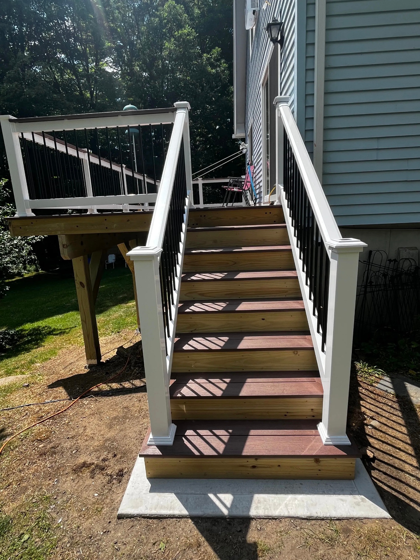 Finished stair descent from the elevated Wolf composite deck in Nottingham NH with white railing and black aluminum balusters